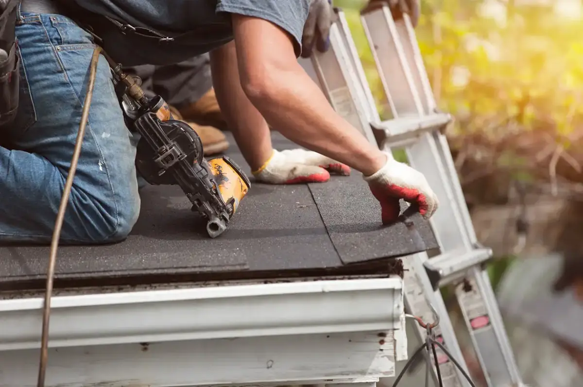 Roofer using a nail gun to install asphalt shingles on a sloped roof